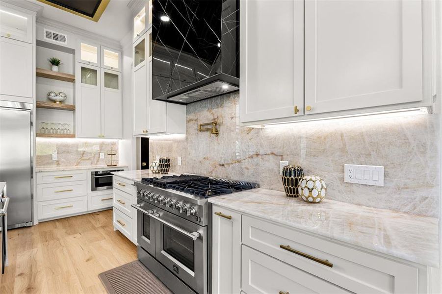 Gourmet kitchen featuring a professional-grade gas range, built-in microwave, under-cabinet lighting, and light-toned cabinetry with gold-finish hardware