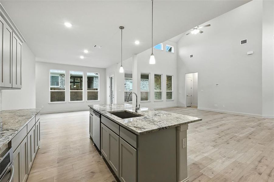 Kitchen featuring gray cabinetry, open floor plan, light stone counters, light wood-type flooring, and high vaulted ceiling