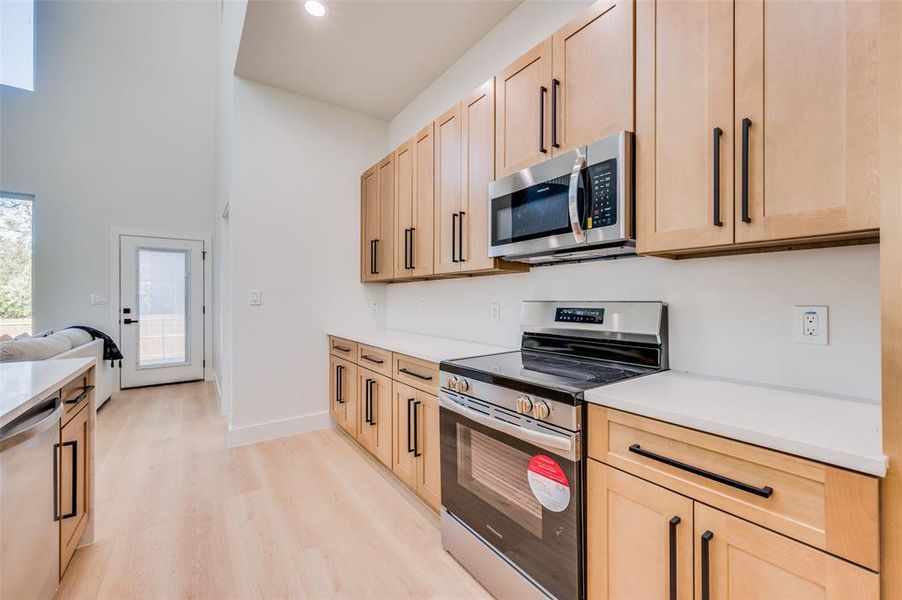 Kitchen with light brown cabinetry, light wood-type flooring, and appliances with stainless steel finishes