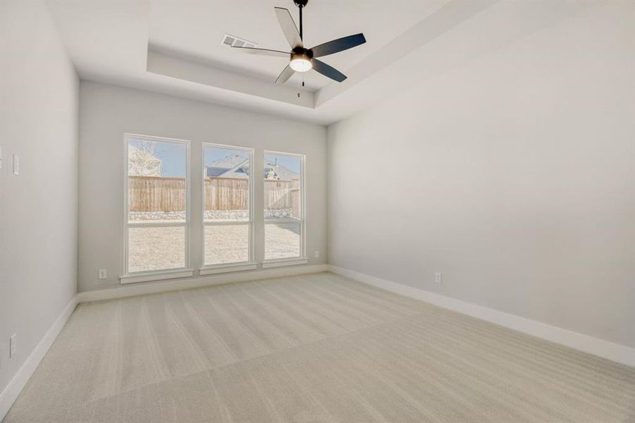 Empty room featuring light carpet, ceiling fan, and a tray ceiling