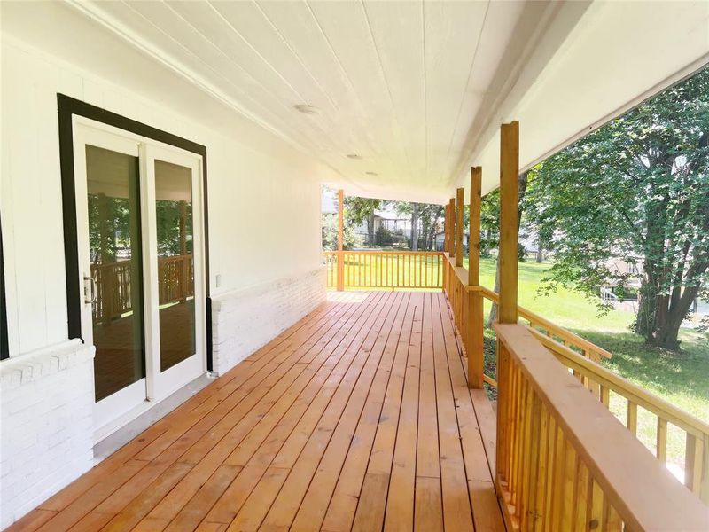 Expansive covered porch featuring natural wood decking, sturdy wood railings, and a white brick facade