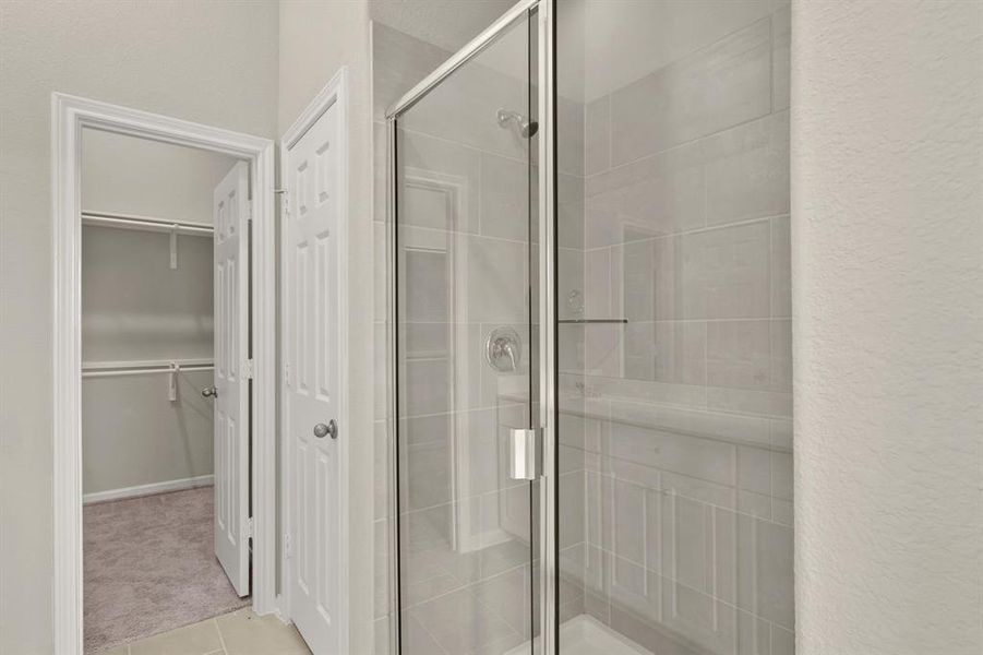 This additional view of your primary bathroom features tile flooring, fresh paint, walk-in shower, and a large walk-in closet.