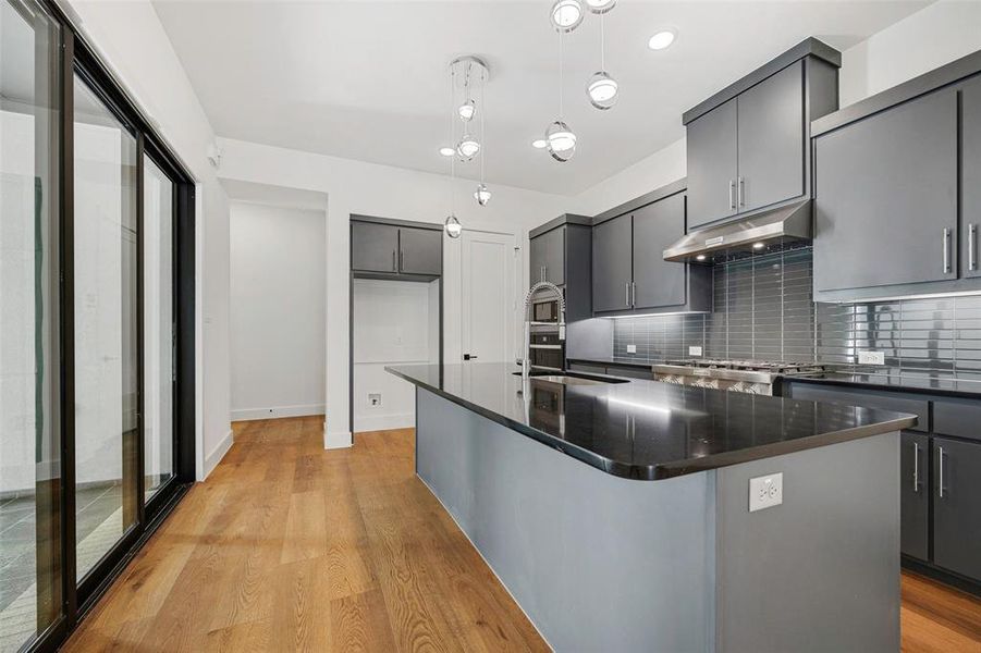 Kitchen with decorative light fixtures, decorative backsplash, light wood-type flooring, range, and under cabinet range hood