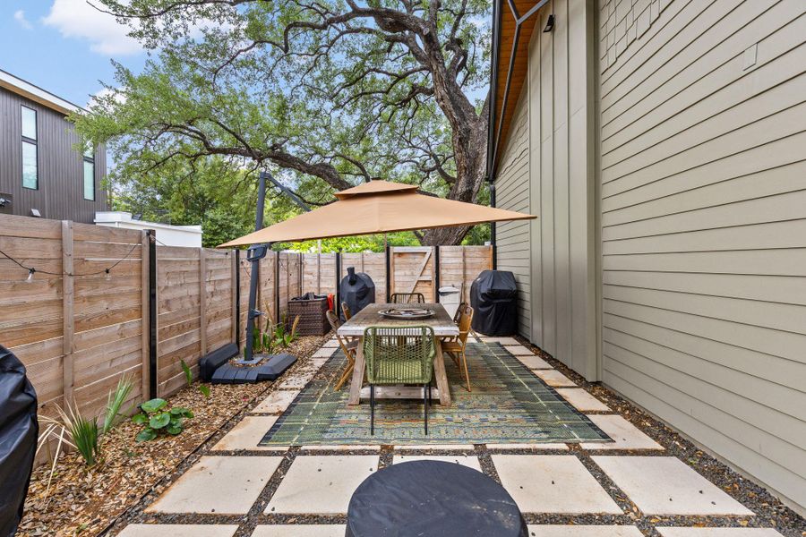 An inviting backyard patio offers a perfect spot for al fresco dining, shaded by a large umbrella and mature trees. An inviting backyard patio offers a perfect spot for al fresco dining, shaded by a large umbrella and mature trees.