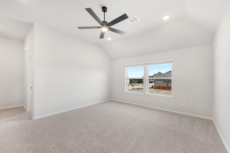 Empty bedroom with vaulted ceiling, ceiling fan, carpet flooring, and a window overlooking neighboring homes. Empty bedroom with vaulted ceiling, ceiling fan, carpet flooring, and a window overlooking neighboring homes.