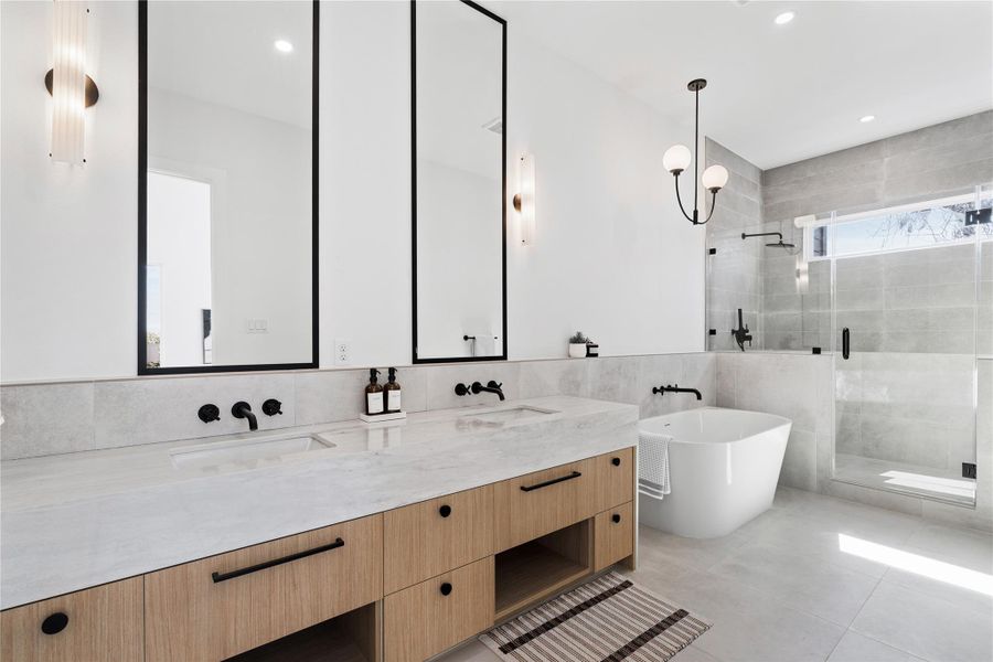 A spa-inspired primary bath showcases a floating double vanity with sleek black fixtures, oversized mirrors, and a freestanding soaking tub set against soft, neutral tile.