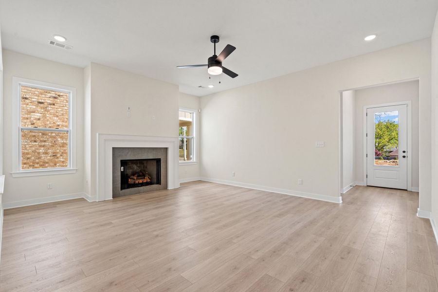 Unfurnished living room featuring a ceiling fan, light wood finished floors, healthy amount of natural light, and a fireplace