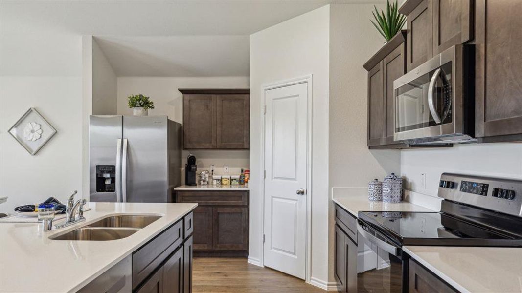 Kitchen with stainless steel appliances, dark wood finish cabinets, dark wood finished floors, and light stone countertops