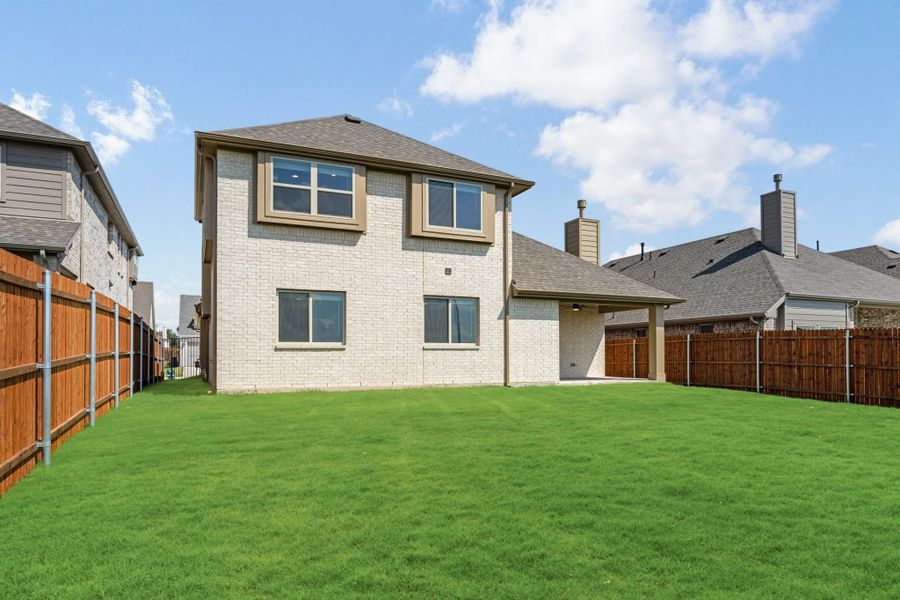 Two-story brick home with covered patio, large green backyard, and wood privacy fence