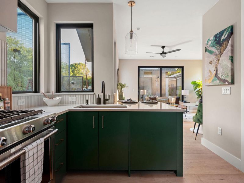 Kitchen with green cabinetry, stainless steel gas stove, light wood finished floors, hanging light fixtures, and a ceiling fan Kitchen with green cabinetry, stainless steel gas stove, light wood finished floors, hanging light fixtures, and a ceiling fan