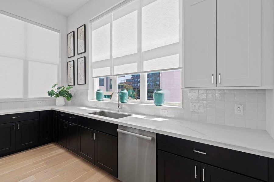 A well-lit kitchen with sleek black cabinetry and white countertops, illuminated by multiple windows. A well-lit kitchen with sleek black cabinetry and white countertops, illuminated by multiple windows.