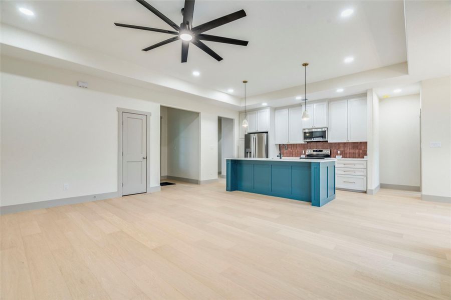Kitchen with open floor plan, white cabinets, pendant lighting, an island with sink, and light countertops