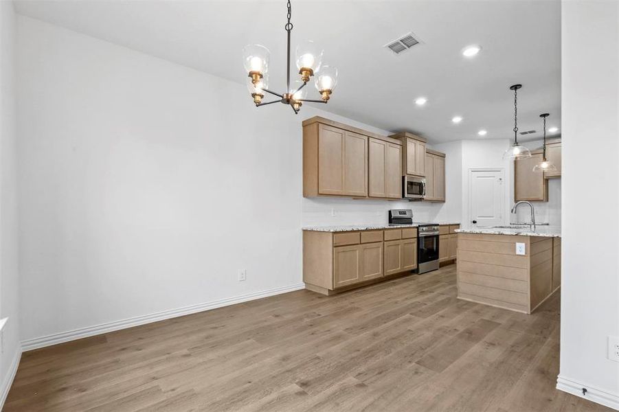 Kitchen with light hardwood / wood-style flooring, light stone countertops, light brown cabinets, appliances with stainless steel finishes, and decorative light fixtures