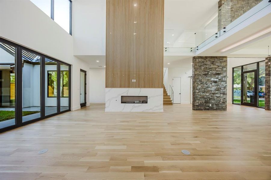 Unfurnished living room with a premium fireplace, a towering ceiling, light wood-type flooring, and recessed lighting Unfurnished living room with a premium fireplace, a towering ceiling, light wood-type flooring, and recessed lighting