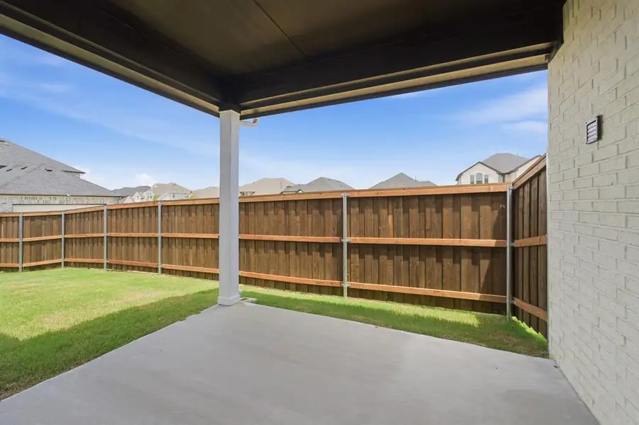 Covered outdoor patio with a concrete slab, white brick exterior, wood privacy fencing, and a manicured lawn