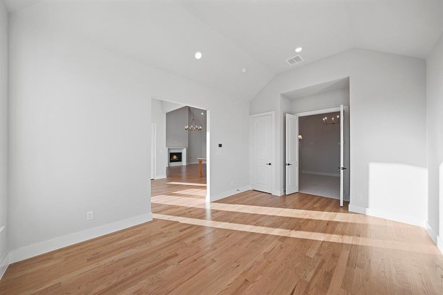 Unfurnished bedroom with a chandelier, light wood-type flooring, vaulted ceiling, a lit fireplace, and recessed lighting Unfurnished bedroom with a chandelier, light wood-type flooring, vaulted ceiling, a lit fireplace, and recessed lighting
