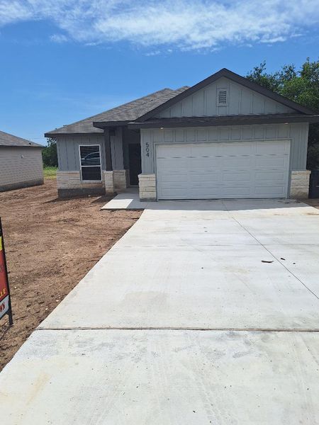 View of front of property featuring driveway, board and batten siding, a garage, roof with shingles, and stone siding