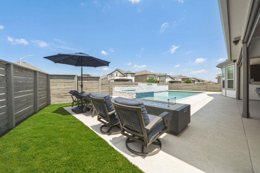 Expansive outdoor living area featuring a swimming pool with a textured accent wall, a wide concrete patio, and a turfed manicured lawn