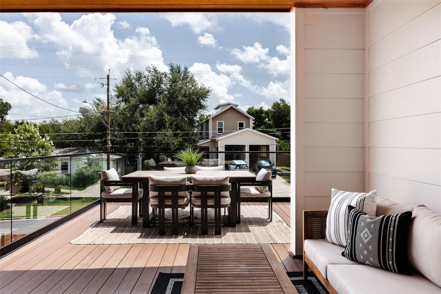 The second-story balcony, with its sleek glass railing, offers unobstructed views and an ideal space for outdoor dining, blending comfort and elegance seamlessly.