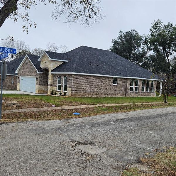 View of side of property with brick siding, a shingled roof, a yard, driveway, and an attached garage