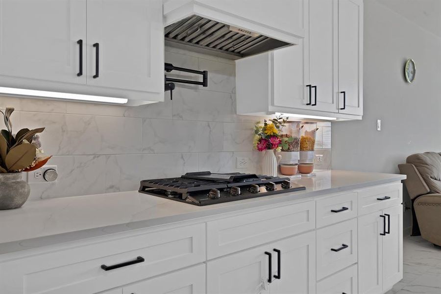 Kitchen featuring gas stovetop, marble finish floor, premium range hood, and white cabinets