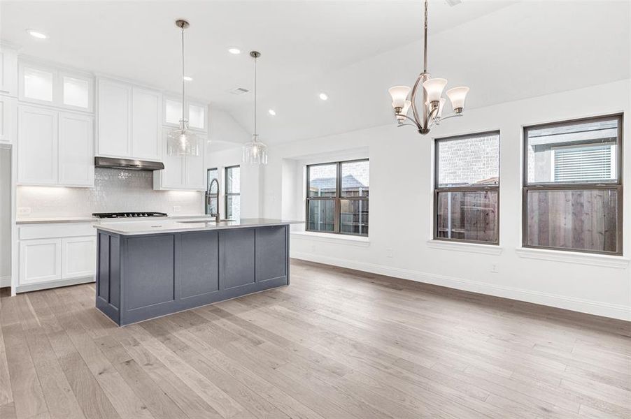 Kitchen featuring white cabinets, a center island with sink, hanging light fixtures, and lofted ceiling