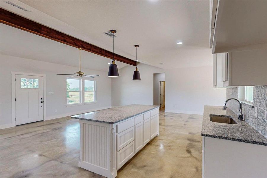 Kitchen featuring pendant lighting, sink, stone counters, vaulted ceiling with beams, and white cabinets