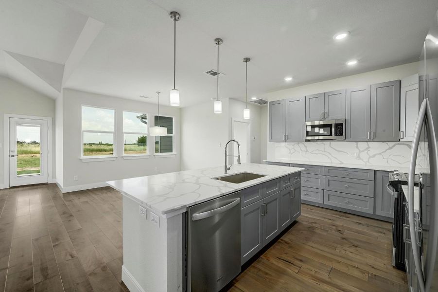 Kitchen with appliances with stainless steel finishes, gray cabinetry, decorative backsplash, light stone counters, and a center island with sink Kitchen with appliances with stainless steel finishes, gray cabinetry, decorative backsplash, light stone counters, and a center island with sink
