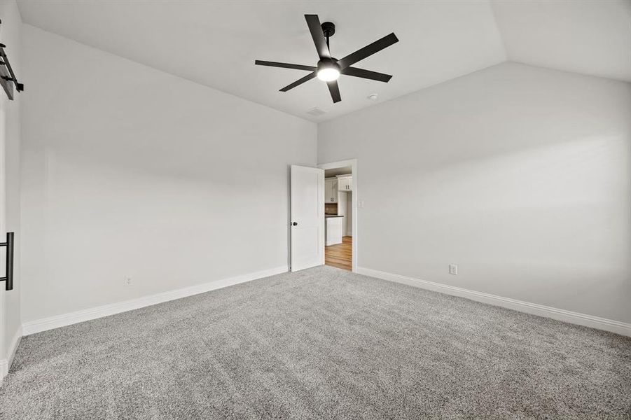 Spare room with light colored carpet, vaulted ceiling, a ceiling fan, and a barn door