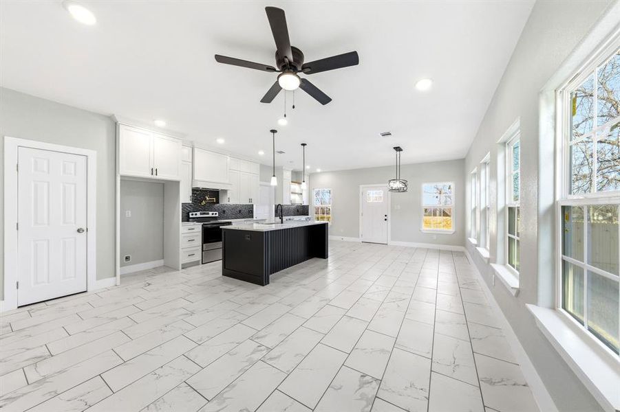 Kitchen featuring a ceiling fan, light marble finish floors, stainless steel range with electric cooktop, white cabinets, and a kitchen island with sink