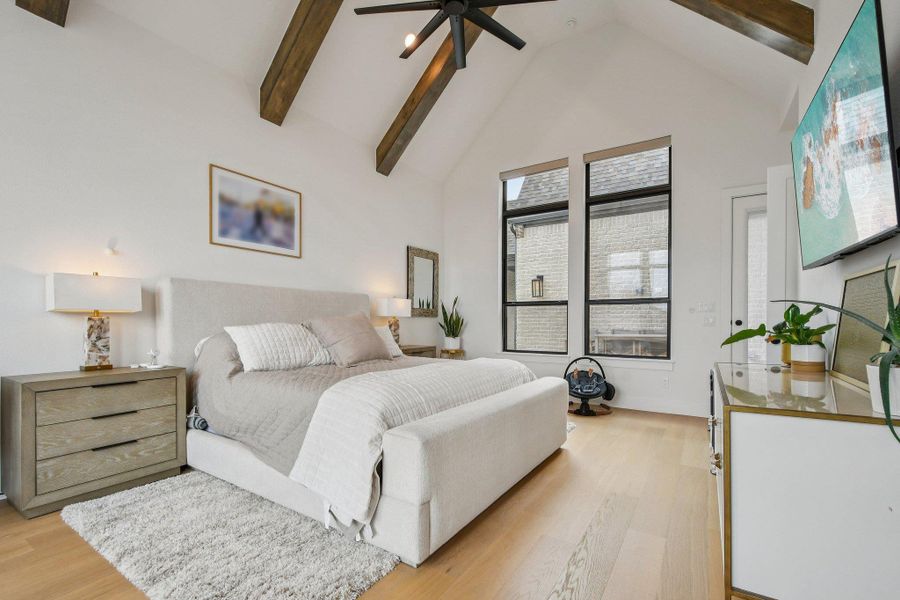 This bedroom features light wood flooring, a vaulted ceiling with exposed wood beams, and a ceiling fan This bedroom features light wood flooring, a vaulted ceiling with exposed wood beams, and a ceiling fan