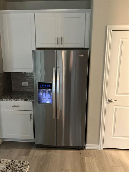 Kitchen with stainless steel fridge with ice dispenser, white cabinetry, light stone countertops, and light wood finished floors