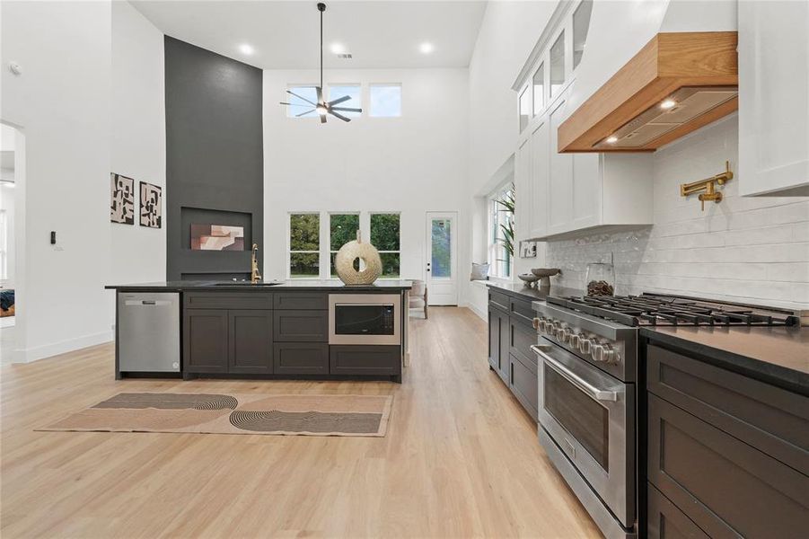 Kitchen featuring appliances with stainless steel finishes, glass insert cabinets, light wood finished floors, white cabinetry, and a high ceiling Kitchen featuring appliances with stainless steel finishes, glass insert cabinets, light wood finished floors, white cabinetry, and a high ceiling