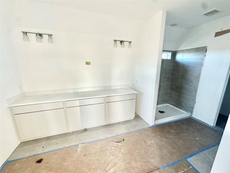 Full bathroom with double vanity, a tile shower, and light tile patterned flooring