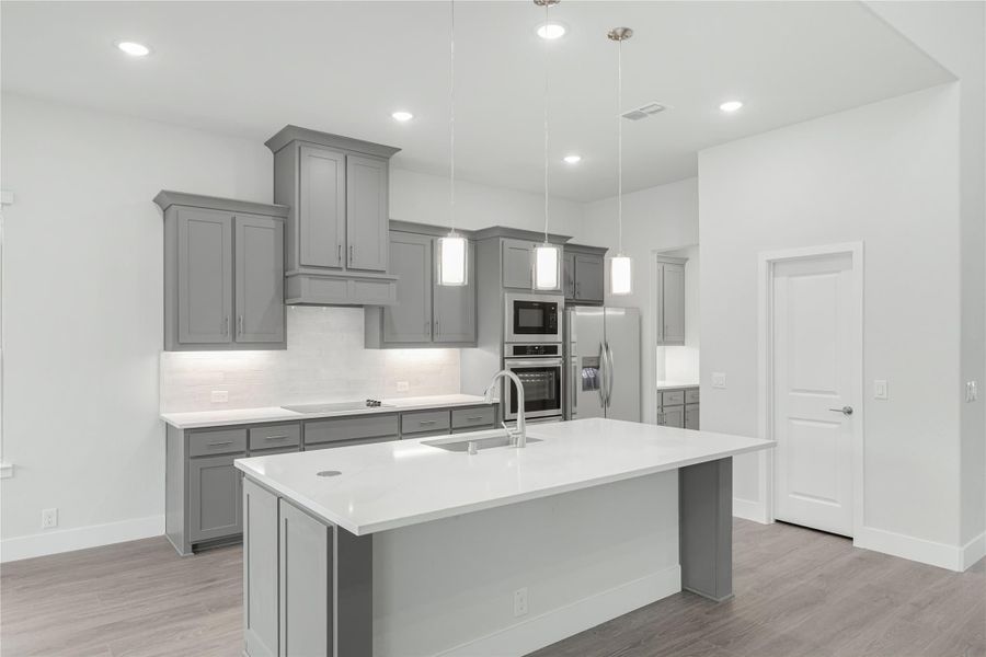 Kitchen with gray cabinets, large center island with sink, stainless steel appliances, and pendant lights overhead.