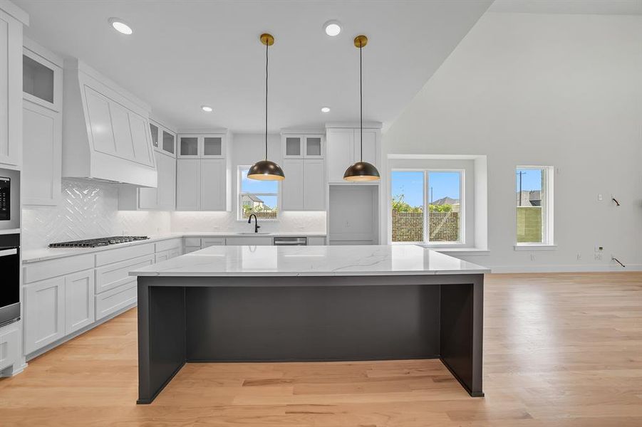 Kitchen with a kitchen island, white cabinetry, glass insert cabinets, light wood-style floors, and high vaulted ceiling