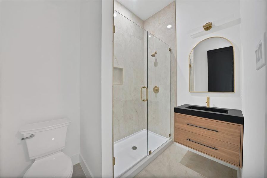 Bathroom featuring a frameless glass shower enclosure, a modern floating vanity with a dark countertop and integrated sink, and an arched mirror
