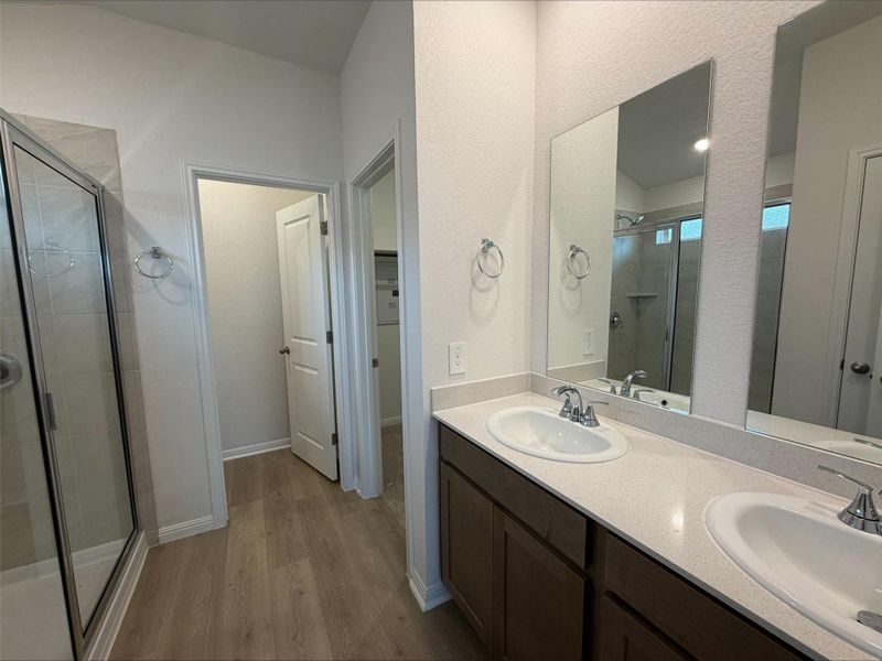 Full bath with a stall shower, dark wood-type flooring, double vanity, and a walk in closet