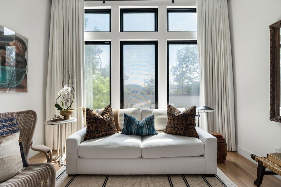 A dedicated sitting area sits within the primary suite, framed by oversized windows and custom drapes that bring in natural light while creating a quiet spot to unwind.