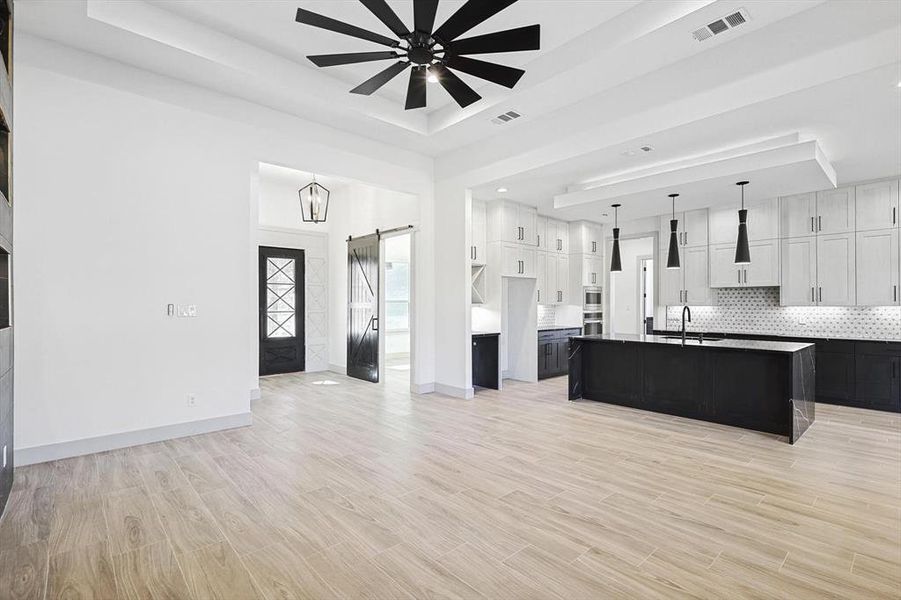 Kitchen featuring a tray ceiling, ceiling fan, a center island with sink, and white cabinets