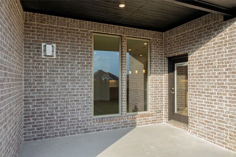 Covered patio with brick walls, large window, and dark-framed door on concrete floor