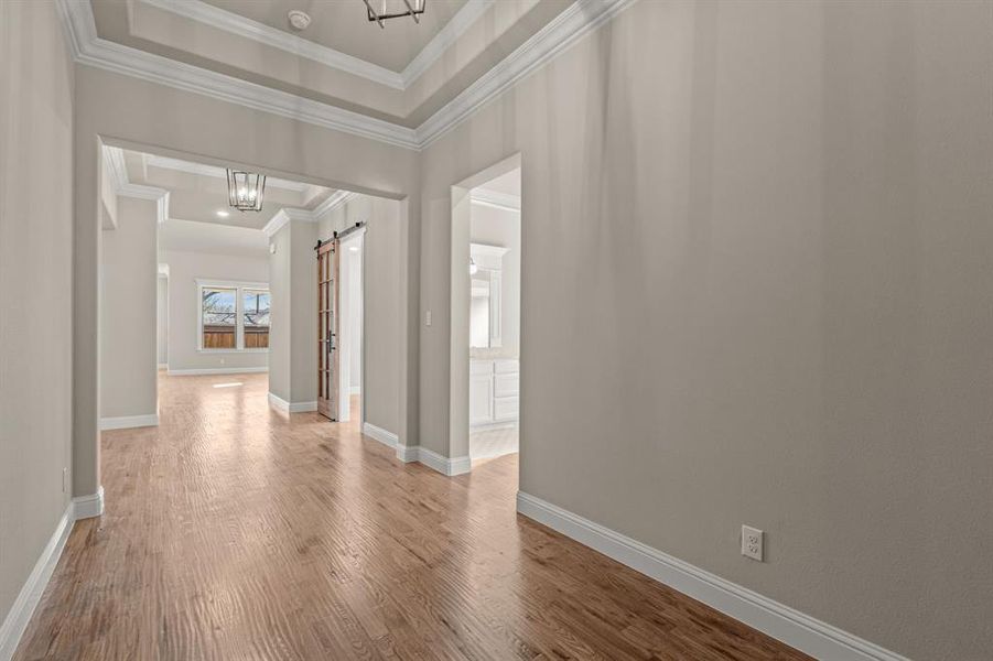 Hallway with ornamental molding, a barn door, a chandelier, and wood-type flooring