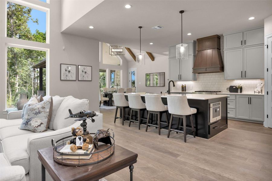The kitchen showcases a spacious, maple wood island with seating, unbelievable Weisenbaker cabinetry, a custom Beechwood vent hood (stained Hazelnut) and elegant pendant lighting—all seamlessly connected to the main living space.