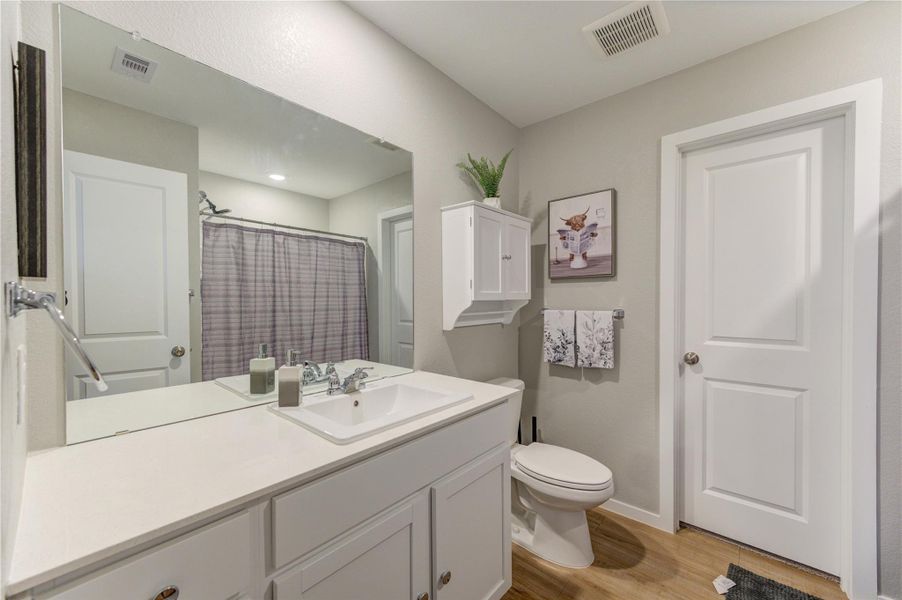 This bathroom features a clean, modern design with a large mirror, white cabinetry, and a single sink. It has a shower with a curtain, wood-look flooring, and neutral wall colors, creating a fresh and inviting space.