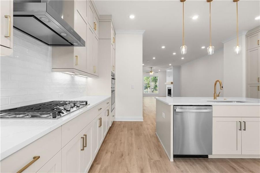 Kitchen featuring wall chimney exhaust hood, appliances with stainless steel finishes, open floor plan, light wood-type flooring, and tasteful backsplash