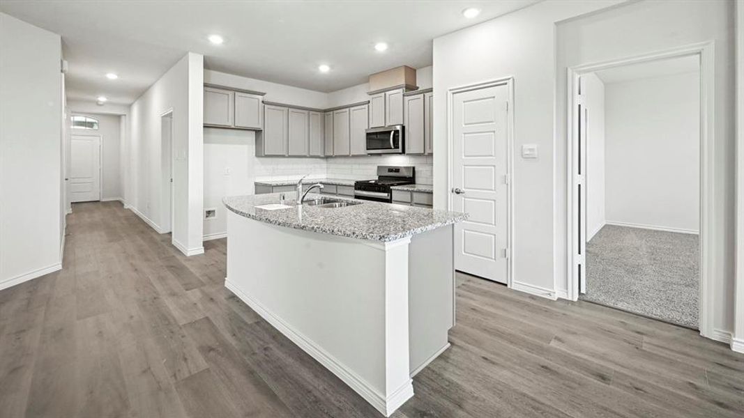 Kitchen featuring a curved island with an undermount sink, granite countertop, and gray cabinetry