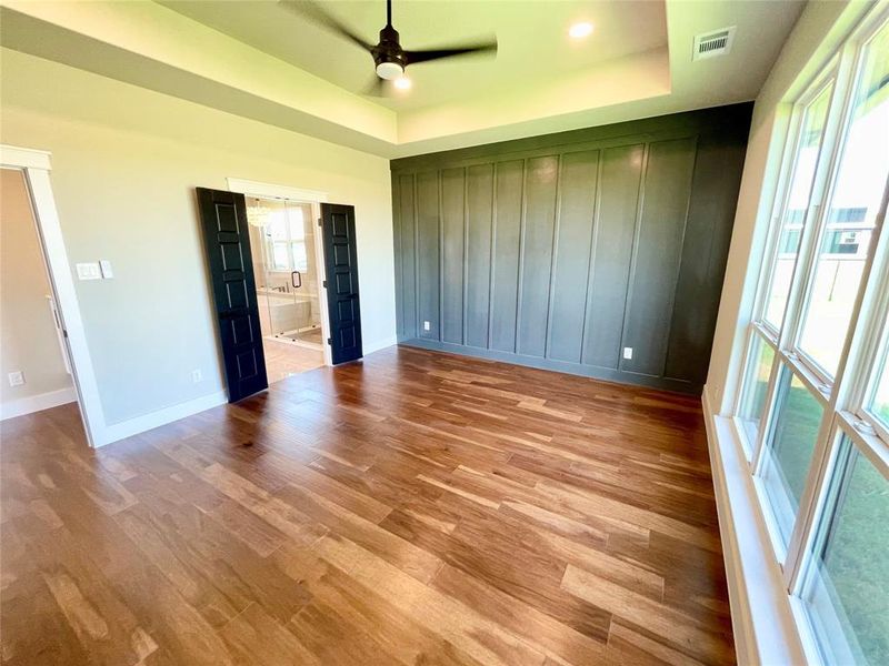 Unfurnished bedroom featuring ceiling fan, a raised ceiling, connected bathroom, and light hardwood / wood-style flooring