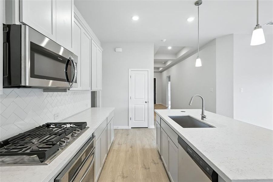 Kitchen featuring light wood-style flooring, stainless steel appliances, pendant lighting, light stone countertops, and recessed lighting Kitchen featuring light wood-style flooring, stainless steel appliances, pendant lighting, light stone countertops, and recessed lighting