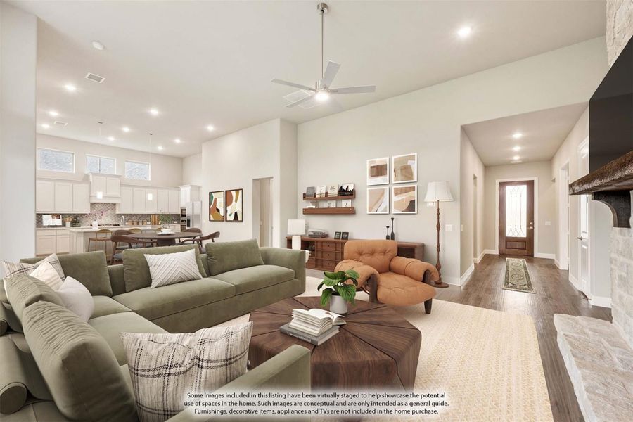 Open-concept living room with high ceilings, ceiling fan, stone fireplace, and view into kitchen and entryway