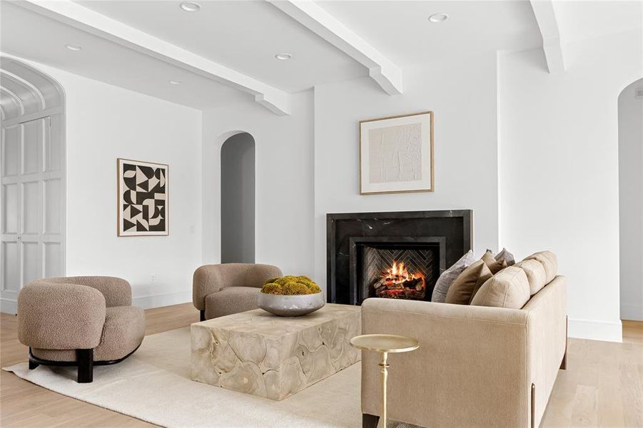 Sitting room with arched walkways, light wood-style floors, beamed ceiling, a lit fireplace, and recessed lighting